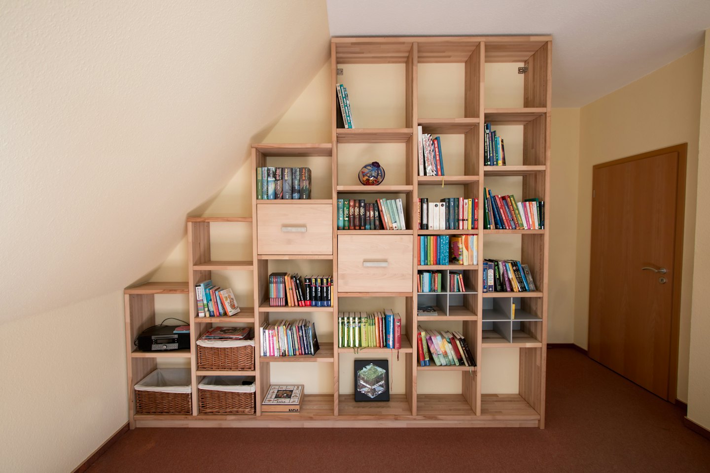Maßgefertigtes Bücherregal aus Holz unter einer Dachschräge, gefüllt mit Büchern.